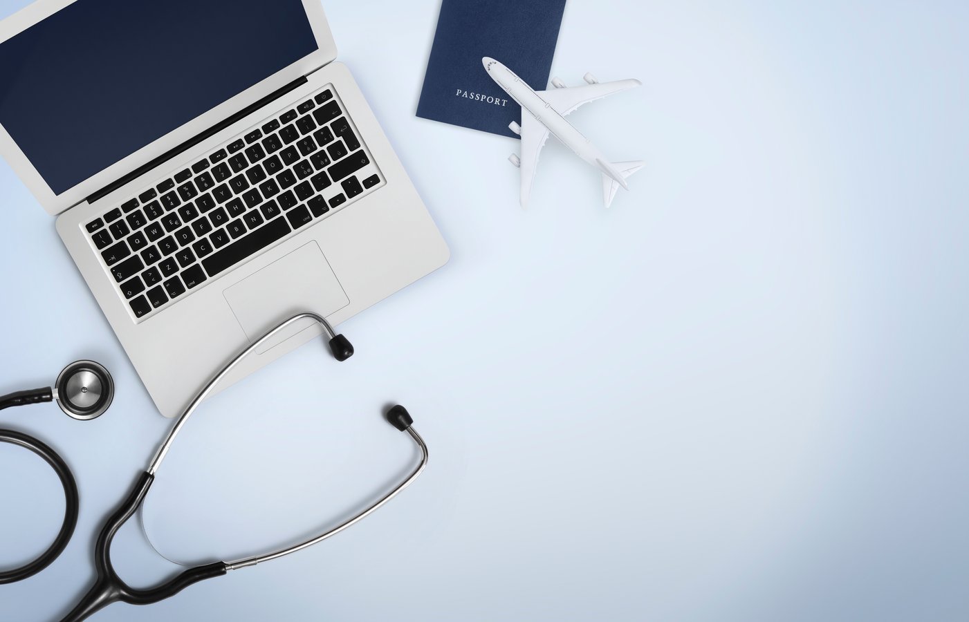Reiseversicherungen für den Urlaub: Stethoskop, Laptop, Miniaturflugzeug mit Reisepass im Hintergrund.