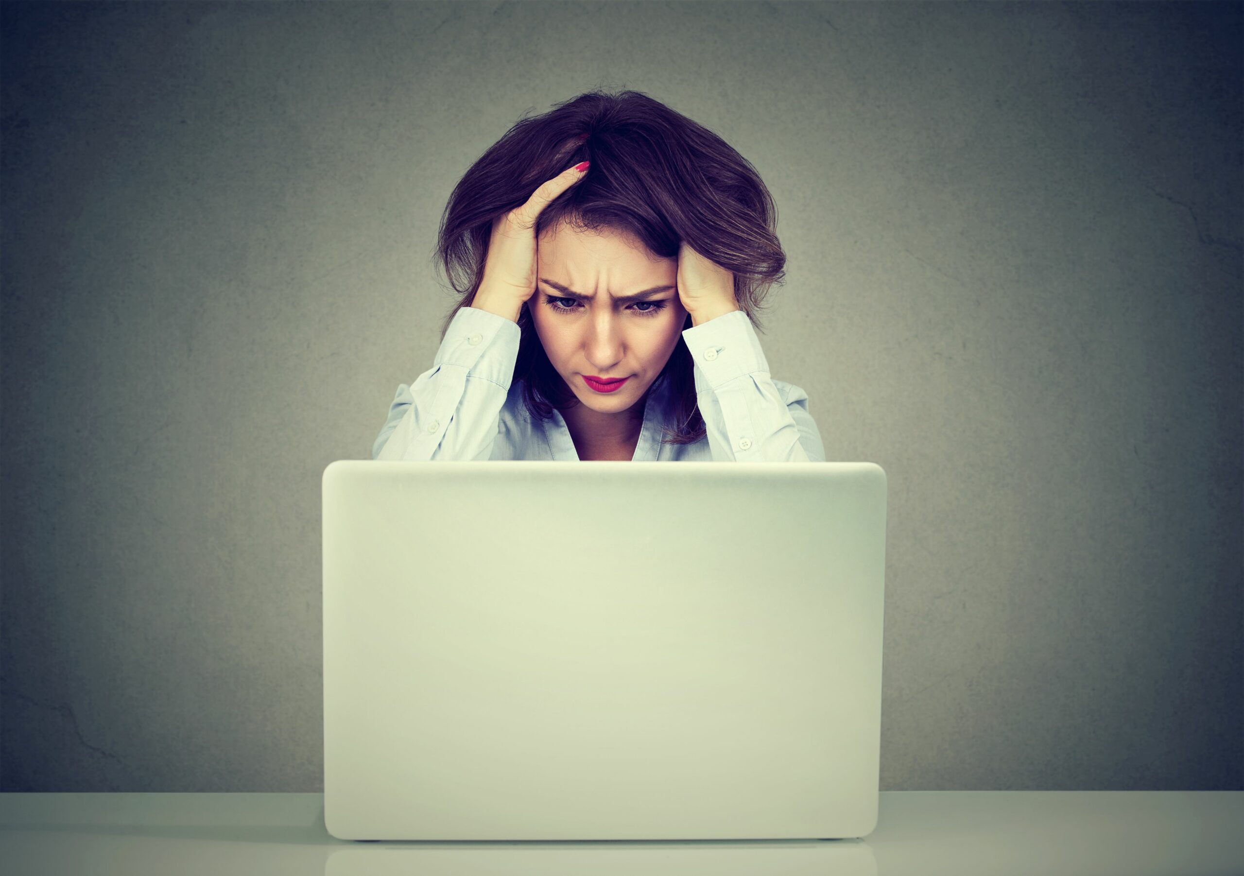 Eine Frau starrt gestresst auf den Lapropbildschirm vor ihr.
