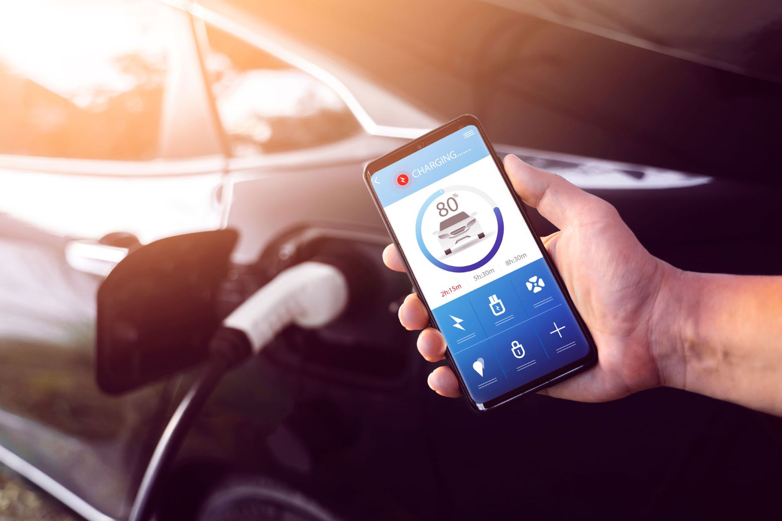 E-Autobesitzer hält Smartphone mit geöffneter Lade-App, im Hintergrund lädt das Auto