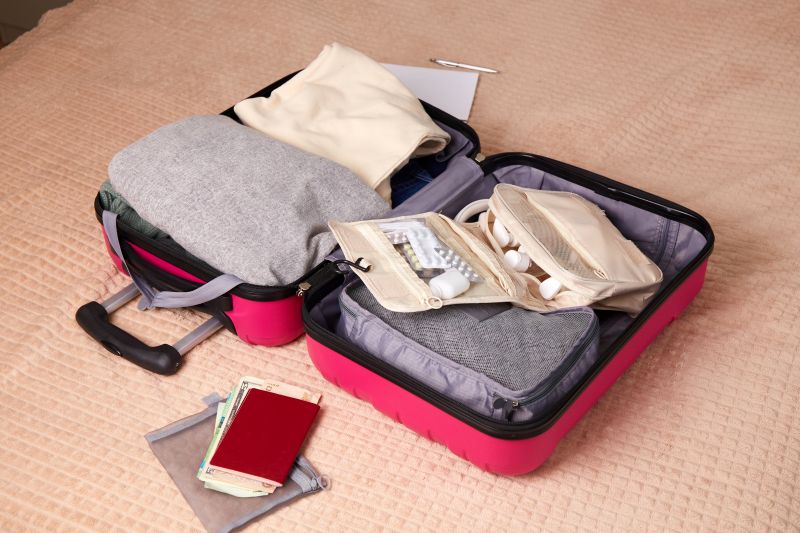 In einem rosa Reisekoffer stapeln sich Kleidung, Papiere und eine Reiseapotheke.